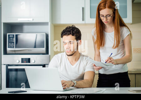 Donna calcolare o scrivere i conti con penna, suo marito utilizzando laptop Foto Stock