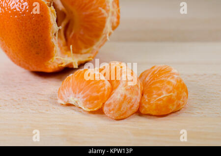 Segmenti di mandarino e mandarino intero su un tavolo di legno Foto Stock