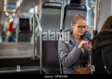 Piuttosto, giovane donna su un tram/tram, durante il suo tragitto al lavoro. Utilizzando il suo smartphone. (Colore immagine dai toni shallow DOF) Foto Stock