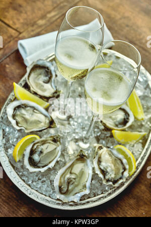 Chiudere fino a ostriche istituito intorno silver platter riempito con ghiaccio tritato, le fette di limone e calici di champagne in medio Foto Stock