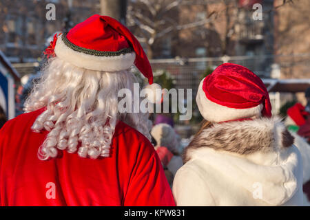 Vista posteriore di un uomo che indossa una santa claus costume in piedi accanto a una donna che indossa un cappello di Natale Foto Stock