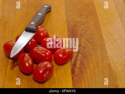 Numerosi mini pomodori ciliegia su un tagliere di legno con un coltello appoggiato su di essi Foto Stock