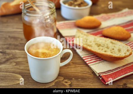 Il dolce miele nel vasetto di vetro e caffè caldo, il pane e la torta su una tovaglia rustico e lo sfondo di legno Foto Stock