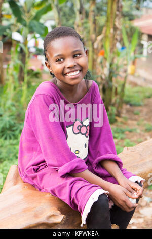 Una bella risata ragazza ugandese seduto su un albero caduto trunk. Foto Stock