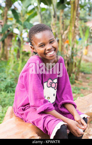 Una bella risata ragazza ugandese seduto su un albero caduto trunk. Foto Stock