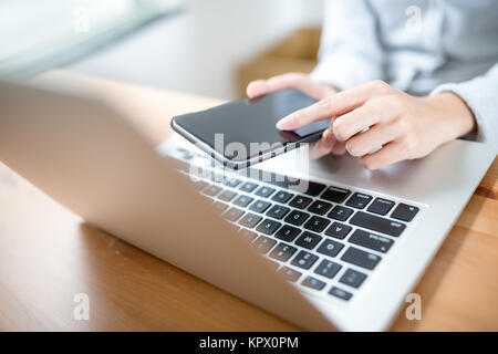 Donna mano toccare telefono sulla tastiera del notebook Foto Stock