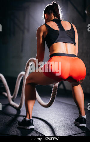 Vista posteriore della donna facendo attraversare montare esercizio con funi di battaglia Foto Stock