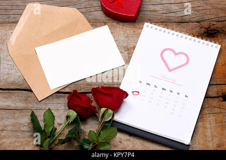 Calendario che mostra la data 14 febbraio. Red Rose, cuori e confezione regalo su un tavolo di legno. Foto Stock