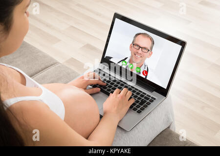 Donna incinta la videoconferenza con medico sul computer portatile Foto Stock