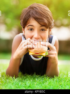 Teen boy burger di mangiare all'aperto Foto Stock