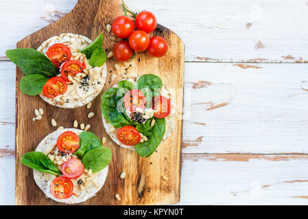 Snack sani da torte di riso con hummus, spinaci e pomodori in luce sullo sfondo di legno Foto Stock