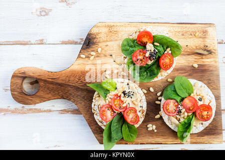 Snack sani da torte di riso con hummus, spinaci e pomodori in luce sullo sfondo di legno Foto Stock