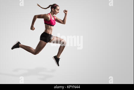 Colpo di una sportiva giovane donna corrono e saltando contro uno sfondo grigio Foto Stock