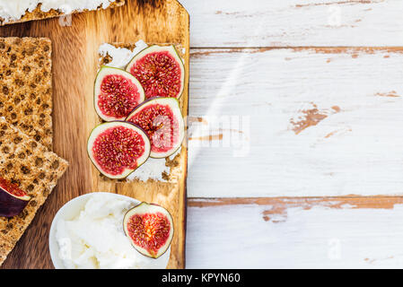 Snack sani dalla segale integrale fette biscottate crackers, fichi e ricotta su luce sullo sfondo di legno Foto Stock