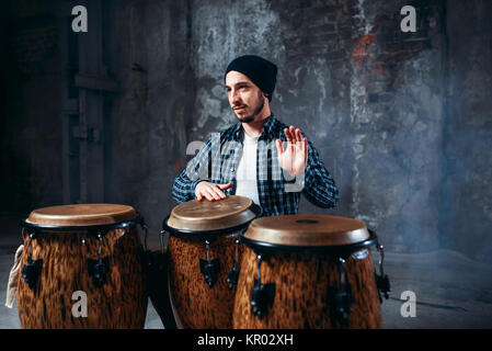 Il batterista giocando sul bongo in legno fusti nel negozio della fabbrica, battere il ritmo, il musicista in movimento. Djembe, musicale strumento a percussione Foto Stock