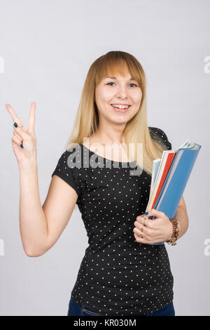 La gioiosa ragazza con una cartella nelle sue mani mostra gesto &QUOT Victoria&QUOT vittoria mano Foto Stock