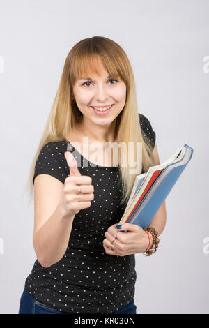 Giovane donna con le cartelle in mani felicemente sorridente e mostrando il pollice Foto Stock