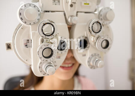 Paziente femmina cerca attraverso phoropter durante esame oculistico Foto Stock