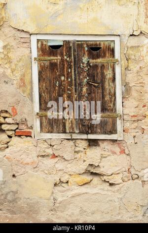 Vecchia finestra in legno con persiane chiuse in una casa diroccata in bisogno di un rinnovo Foto Stock