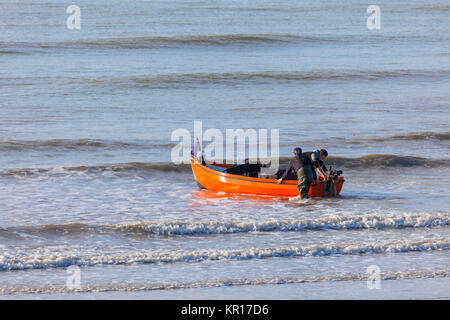 Due giovani uomini lanciando una piccola barca in mare in Hastings Foto Stock