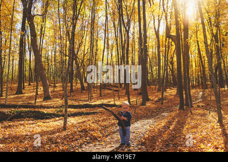 Ragazzo in piedi su un sentiero forestale tenendo un bastone Foto Stock