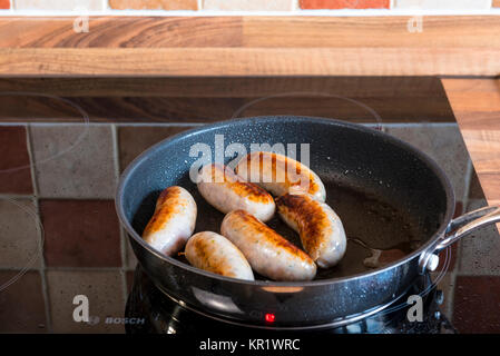 Salsicce una cottura in padella su di un piano di cottura ad induzione. Foto Stock