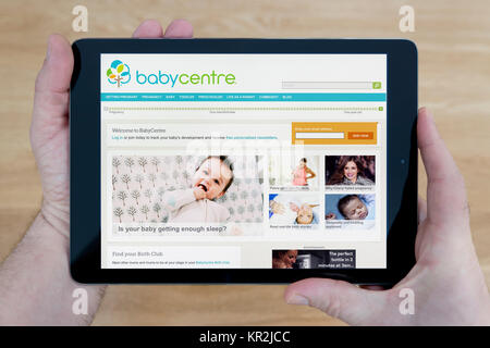 Un uomo guarda al Baby Center sito web sul suo iPad dispositivo tablet, sparato contro un tavolo di legno top sfondo (solo uso editoriale) Foto Stock