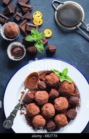 Tartufi di cioccolato fondente sulla piastra bianca decorata con foglia di menta e cioccolato fondente in pezzi. Vista superiore Foto Stock