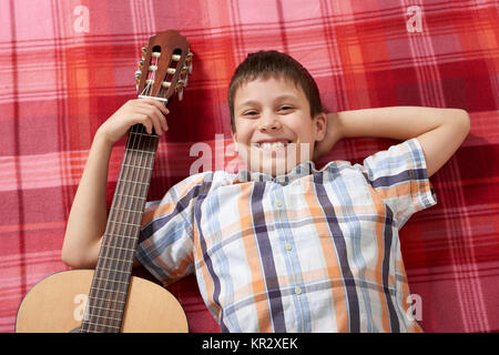 Ragazzo la riproduzione di musica di chitarra, giace su un rosso a scacchi blanket, vista dall'alto Foto Stock