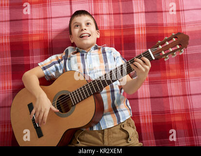 Ragazzo la riproduzione di musica di chitarra, giace su un rosso a scacchi blanket, vista dall'alto Foto Stock