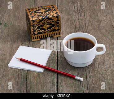 Scrigno, caffè in una tazza bianca e carta con una matita, una vita ancora su un vecchio tavolo Foto Stock