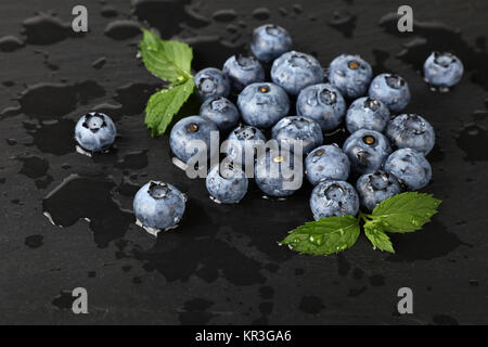 Chiudere di nuovo lavato mirtillo bacche con gocce di acqua e verde menta foglie sul nero ardesia bordo, ad alto angolo di visione Foto Stock