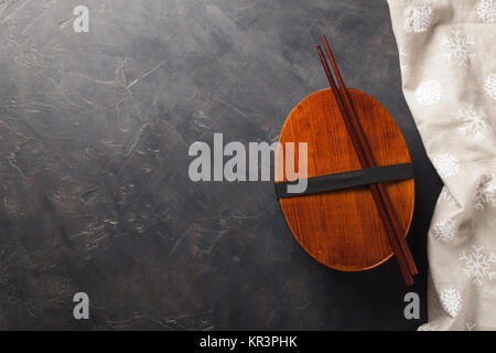 Chiuso in legno lunchbox giapponese con bacchette, su una pietra scura tabella. Vista da sopra con copia spazio. Foto Stock