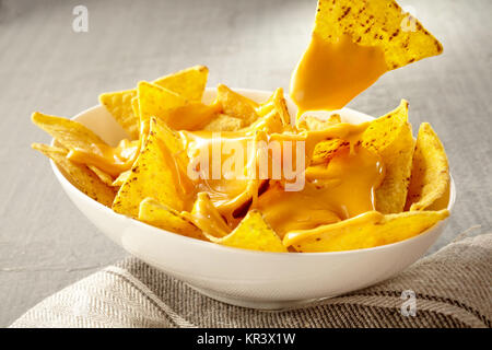 Unico giallo triangolare tortilla di mais chip tirato fuori del recipiente di formaggi oggetto nachos su grigio e tovaglia bianca Foto Stock