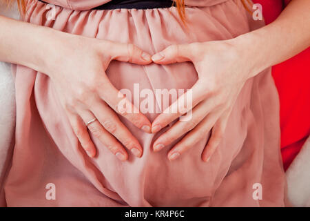Donna incinta tenendo le sue mani a forma di cuore sul suo bambino bump. Pancia in gravidanza con le dita il simbolo del cuore. Concetto di maternità. Baby Shower Foto Stock
