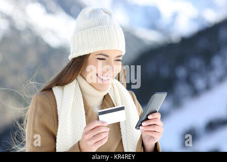 Donna di pagare on line con carta di credito e smart phone in vacanze invernali in una montagna innevata Foto Stock