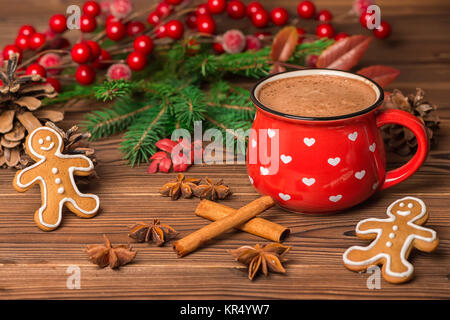 Cioccolata calda e biscotti di panpepato decorate di bacche rosse, albero di Natale ramo, coni, cannella e anis su sfondo di legno, biglietto di auguri Foto Stock