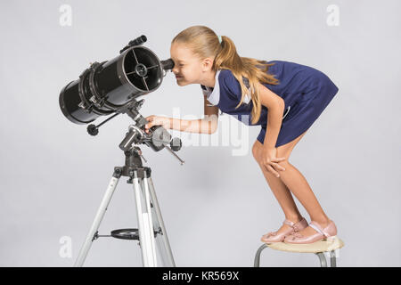Sette anni di ragazza in piedi su una sedia e sembra ridicolo nell'oculare del telescopio riflettore Foto Stock