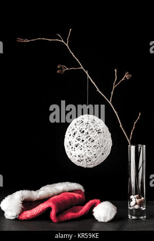 Ramo di ontano in vetro con un bianco Natale palla e santa claus hat sulla pietra nera tabella Foto Stock