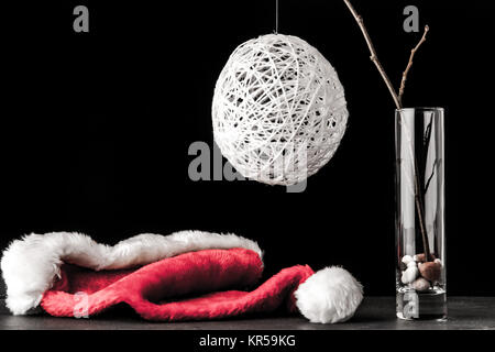 Ramo di ontano in vetro con un bianco Natale palla e santa claus hat sulla pietra nera tabella Foto Stock