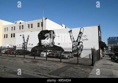 Murale sul muro del magazzino parcheggio, giovane uomo che tiene in su Mani dita V segno guardando sopra le auto nel centro di Los Angeles, California, USA, KATHY DEWITT Foto Stock