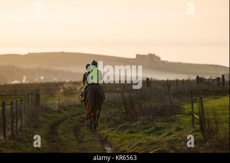 Brighton, East Sussex. 19 dicembre 2017. Regno Unito Meteo. La mattina presto dog walker e cavalieri a Brighton Racecourse e Sheepcote Valley testimonianza un incredibile tramonto sul South Downs National Park in un freddo gelido e mattina sulla costa sud. Credito: Francesca Moore/Alamy Live News Foto Stock