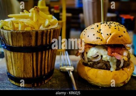 Gustano un delizioso hamburger con cipolle, bacon, formaggio blu e succosa carne di Bangkok. Sideorder: una benna di patatine fritte Foto Stock