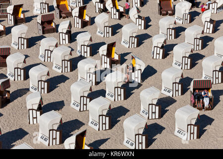 Angolo di alta vista di righe di coperto e sedie da spiaggia in vimini su di una spiaggia di sabbia. Foto Stock