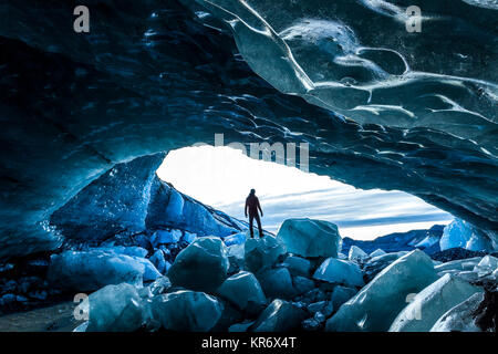 Vista posteriore silhouette di persona in piedi sulla roccia di ghiaccio all'entrata di un ghiacciaio di grotta di ghiaccio. Foto Stock