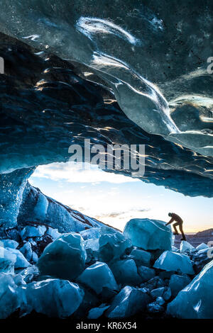 Vista laterale della persona salendo su ghiaccio rock all'entrata di un ghiacciaio di grotta di ghiaccio. Foto Stock