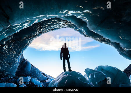Vista posteriore silhouette di persona in piedi sulla roccia di ghiaccio all'entrata di un ghiacciaio di grotta di ghiaccio. Foto Stock