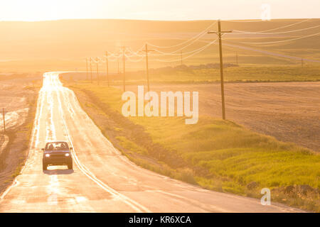 Automobile che viaggia sul lungo rettilineo di autostrada aperta al tramonto.