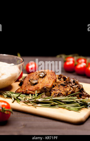 Ai ferri Bistecca di carne di maiale, funghi pomodori ciliegia e una piastra con pasta di fagiolo sul piatto di legno su un tavolo in studio foto su sfondo nero Foto Stock