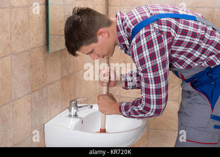 Plumber utilizzando lo stantuffo nel lavandino del bagno Foto Stock